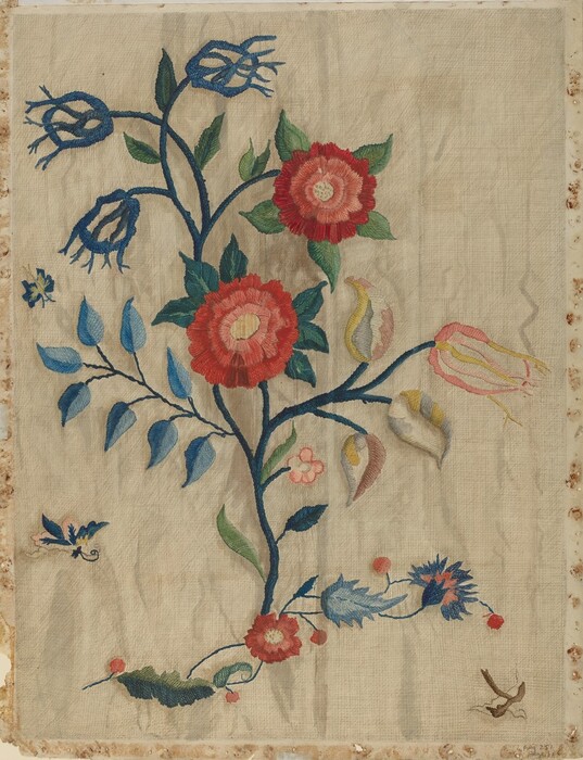 The image displays an embroidered design featuring a large flowering plant with red flowers and various other floral and leaf elements. The color palette includes vibrant reds, greens, blues, yellows, and pinks against a light, neutral background. Central to the fabric, the large red flowers are the focus, with stems and leaves extending in different directions. Additional small flowers and a bird are embroidered around the main plant.