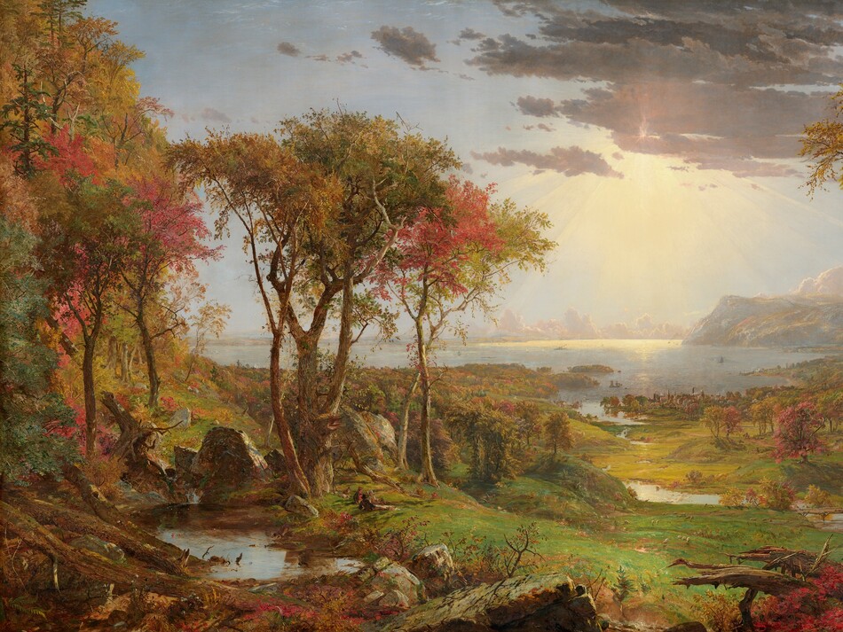 We look out onto a sweeping, panoramic view with trees, their leaves fiery orange and red, framing a view of a distant body of water under a sun-streaked sky in this long, horizontal landscape painting. The horizon comes about halfway up the composition, and is lined with hazy mountains and clouds in the deep distance. Close examination slowly reveals minuscule birds tucked into the crimson-red, golden yellow, and deep, sage-green leaves of the trees to either side of the painting. Closest to us, vine-covered, fallen tree trunks and mossy gray boulders line the bottom edge of the canvas. Beyond a trickling waterfall and small pool near the lower left corner, and tiny within the scale of the landscape, a group of three men and their dogs sit and recline around a blanket and a picnic basket, their rifles leaning against a tree nearby. The land sweeps down to a grassy meadow crossed by a meandering stream that winds into the distance, at the center of the painting. Touches of white and gray represent a flock of grazing sheep in the meadow. A low wooden bridge spans the stream to our right, and a few cows drink from the riverbank. Smoke rises from chimneys in a town lining the riverbank and shoreline beyond, and tiny white sails and steamboats dot the waterway. Light pours onto the scene with rays like a starburst from behind a lavender-gray cloud covering the sun, low in the sky. The artist signed the painting as if he had inscribed the flat top of a rock at the lower center of the landscape with his name, the title of the painting, and date: “Autumn – on the Hudson River, J.F Cropsey, London 1860.”
