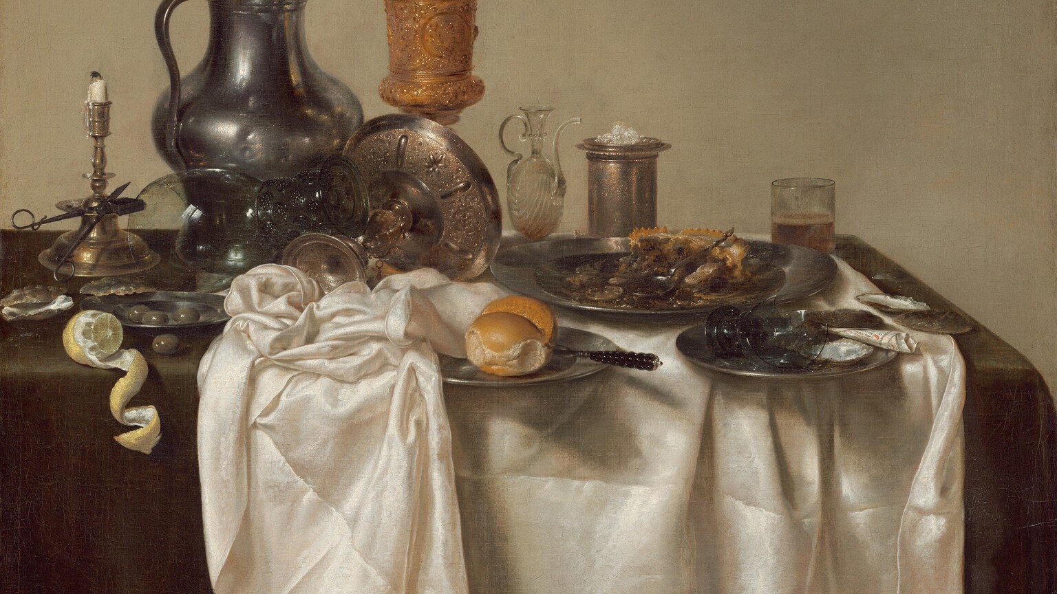 A jumble of pewter plates and a pitcher, glass goblets, a gold chalice, a brass candlestick, and other vessels along with lemons, olives, and the remains of a mince pie are arranged on a cream-white tablecloth bunched on a dark green tabletop in this square still life painting. The scene is painted almost entirely in shades of cool grays, gold, brown, and white against a deep beige background. The objects span width of the canvas across its center. At the left edge of the painting, a vibrant yellow lemon has been cut so its rind curls in a spiral that hangs over the front edge of the table. Behind the lemon, a scissor-like candle snuffer is propped against the wide ledge of the tall brass candlestick, its white candle nearly burned down. A few glistening olives sit in a small pewter plate, and one olive sits on the tabletop near the lemon and candlestick. A glass goblet with a wide stem with textured knubs rests upended on an elaborately chased, gold, footed vessel that has been tipped over so its wide shallow bowl faces away from us. The tall pewter pitcher behind this is dented on its rounded body. The lidded gold chalice next to the jug is the tallest object in the painting. Next to the chalice, along the right half of the painting, is a glass oil cruet with a long, curving spout, a tall, cylindrical vessel holding a small pile of salt, and a straight-sided, low glass holding beer. In front of these objects, an untouched bread roll and knife sit on a pewter plate at the center of the composition. The remains of the mince pie with its pastry crust sit on a large pewter plate to our right. In front of it is a smaller plate holding a broken goblet and a piece of black and white paper rolled into a cone. A few empty oyster shells sit on the table to the left and right, near the lemons and mince pie. The artist signed and dated the painting along the edge of the white cloth near the lower right corner: “HEDA 1635.”