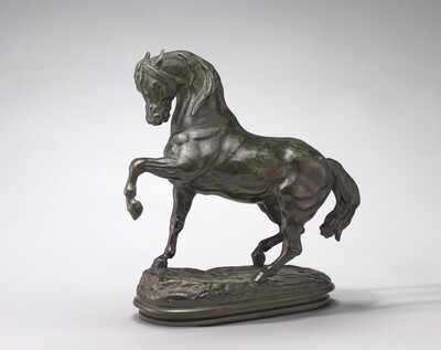 The sculpture depicts a horse in motion with its front left leg raised and its head turned to the side. It is crafted from a dark, metallic material with a green patina. The horse's muscles and contours are detailed, and it stands on a rocky base.