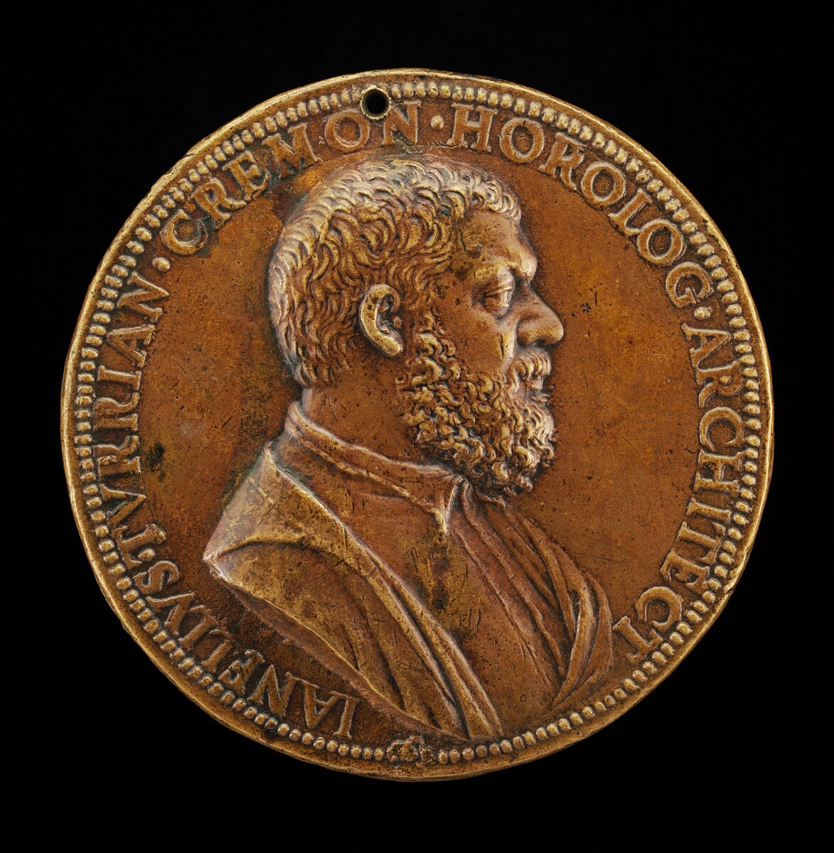 The image depicts a round bronze medallion with a relief sculpture of a man's profile looking to the right. The subject is a male figure with curly, short hair and a full beard. He is depicted wearing a garment with a collar visible at the neckline. The sculpture is rendered in bronze, giving it a warm, golden-brown color with some darker patina. Surrounding the profile is a border with an inscription that reads, "IAN.ELVSJ.VIRIAN.CREMON.HOROLOG.ARCHITECT." A small hole is present at the top of the medallion. The craftsmanship is detailed, providing a realistic portrayal of the subject.