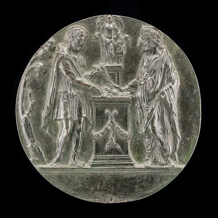 The sculpture is a circular relief depicting two male figures engaged in a handshake over an altar-like structure. One figure is dressed in classical attire, wearing a tunic and a cloak, while the other is similarly robed. In the background, there is a smaller figure or statue on a pedestal. The sculpture is crafted from a material that appears to be silver or a silver-like metal, giving it a shiny and reflective surface. The details are intricately carved, showing the folds in their garments and the expressions on their faces. The sculpture is designed to be viewed from the front, and the deeply carved elements create shadows that highlight the figures' outlines against the circular background.
