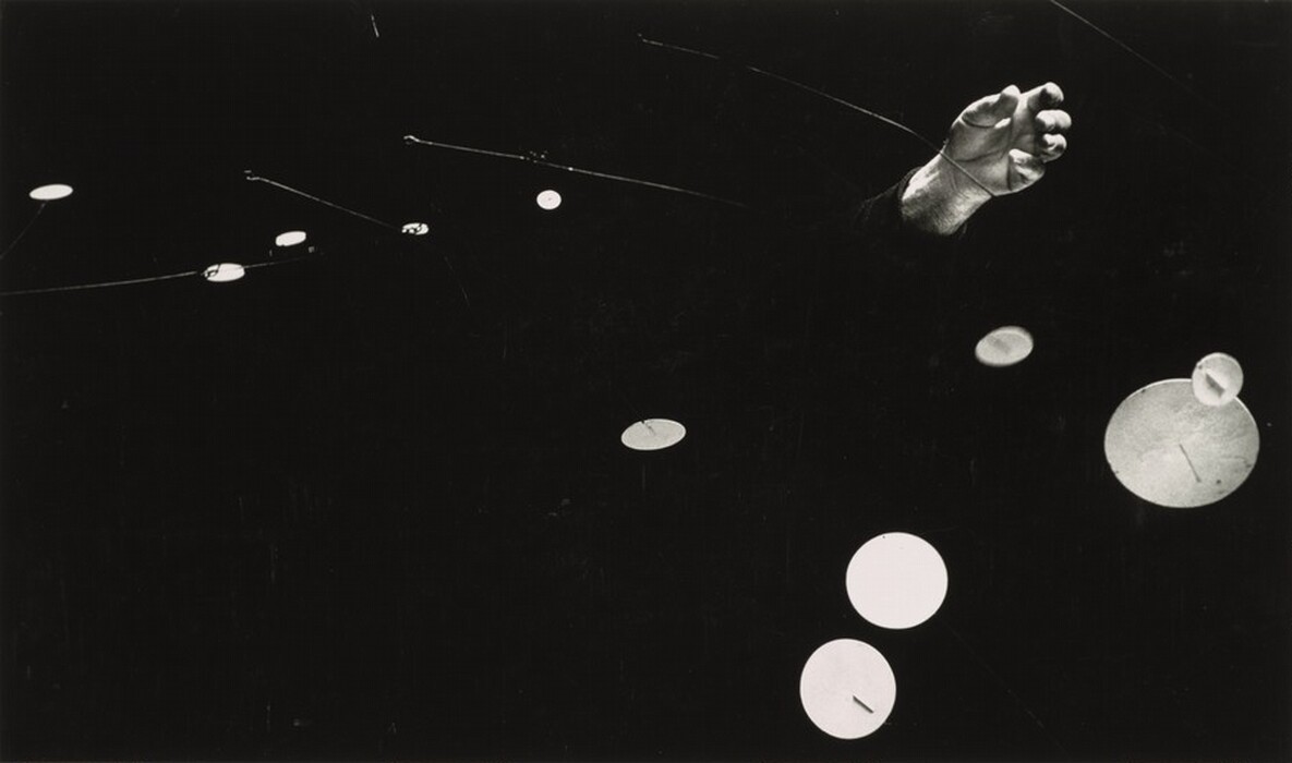 This abstract image features circular shapes connected by thin, linear elements on a dark background. A human hand emerges, adding a human element to the scene. The contrast between the light circles and dark background creates depth.