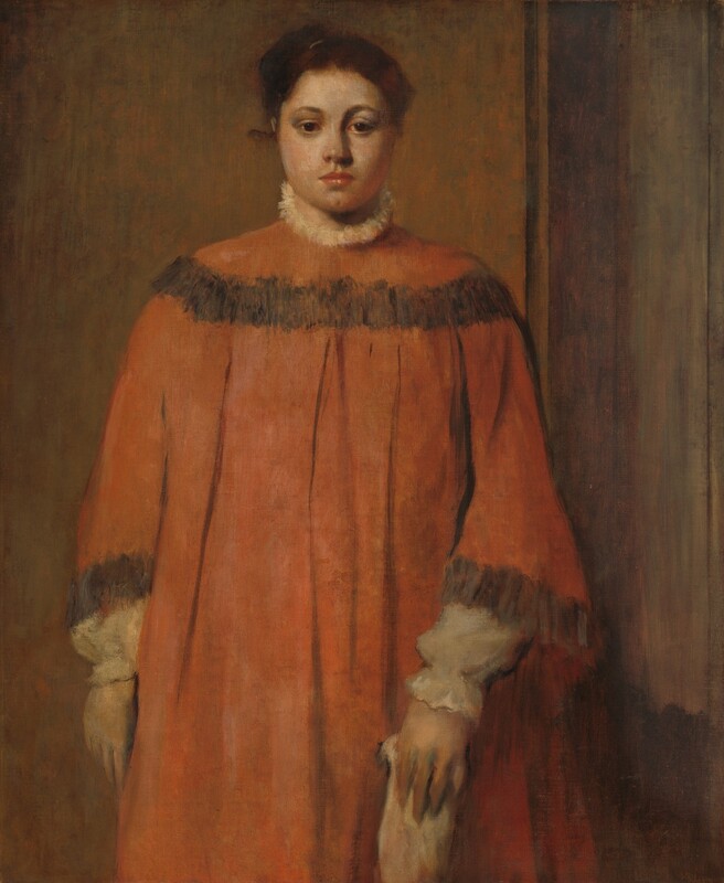 Shown from the knees up, a pale-skinned woman in a voluminous rust-orange dress stands facing us in this vertical portrait painting. She looks toward us but slightly down with dark brown eyes under curved brows. She has a wide face, rounded cheeks, a broad nose, and closed, coral-pink lips over a deeply dimpled chin. Her chestnut-brown hair is pulled up and back. The orange dress has a band of charcoal gray across the shoulders and at the flaring cuffs. Wide, vertical pleats fall from under the band across her chest. White trim, perhaps lace or fur, is suggested by loosely painted cream white at the high neck. The poofy sleeves and cinched cuffs of her white shirt extend beyond the dress sleeves. Her right arm, to our left, hangs by her side and the other holds an indistinct, loosely painted light-colored object down in front of her. She seems to be in a corner with the wall behind thinly washed in muted brown and green and a sienna-brown wood panel wall to our right.