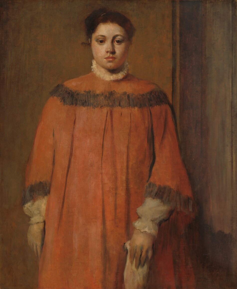 Shown from the knees up, a pale-skinned woman in a voluminous rust-orange dress stands facing us in this vertical portrait painting. She looks toward us but slightly down with dark brown eyes under curved brows. She has a wide face, rounded cheeks, a broad nose, and closed, coral-pink lips over a deeply dimpled chin. Her chestnut-brown hair is pulled up and back. The orange dress has a band of charcoal gray across the shoulders and at the flaring cuffs. Wide, vertical pleats fall from under the band across her chest. White trim, perhaps lace or fur, is suggested by loosely painted cream white at the high neck. The poofy sleeves and cinched cuffs of her white shirt extend beyond the dress sleeves. Her right arm, to our left, hangs by her side and the other holds an indistinct, loosely painted light-colored object down in front of her. She seems to be in a corner with the wall behind thinly washed in muted brown and green and a sienna-brown wood panel wall to our right.