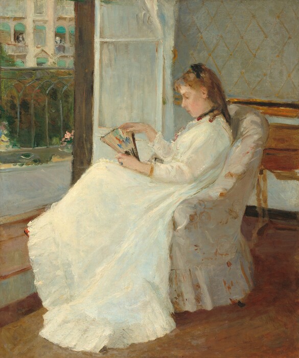 A young woman with pale peach skin and light brown hair sits in profile facing our left in an upholstered chair in this vertical painting. The chair and woman take up most of the composition so seems close to us. She wears a long-sleeved white dress that sweeps to the floor, with black ribbons around her neck and atop her shoulder-length ringlets. The dress has small ruffles at her throat and a deep flounce at the bottom. She gazes down at the partially open fan she holds on her lap. The fan is touched with spots of pumpkin orange, plum purple, and royal blue on a beige background. Loose, swirling brushstrokes in golden tan and bright white against an ivory background suggest that the chair is upholstered with a floral-patterned fabric. A wooden desk or table is pushed against the wall behind the woman to our right and to our left, a white door, covered by a white curtain, opens onto a balcony with a wrought iron railing. Across the street, a couple of people lean out of open windows covered by turquoise-blue awnings on a cream-colored building.