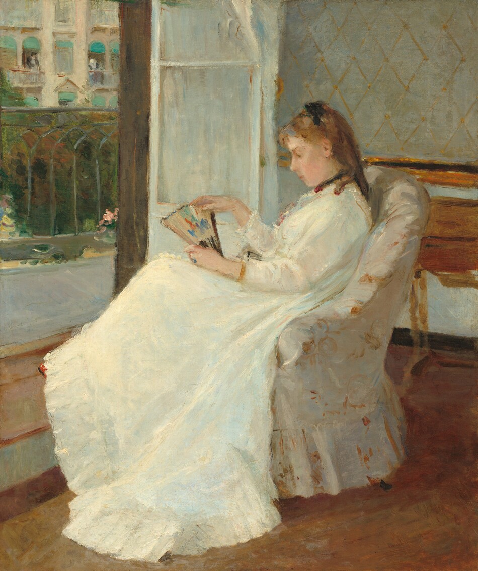 A young woman with pale peach skin and light brown hair sits in profile facing our left in an upholstered chair in this vertical painting. The chair and woman take up most of the composition so seems close to us. She wears a long-sleeved white dress that sweeps to the floor, with black ribbons around her neck and atop her shoulder-length ringlets. The dress has small ruffles at her throat and a deep flounce at the bottom. She gazes down at the partially open fan she holds on her lap. The fan is touched with spots of pumpkin orange, plum purple, and royal blue on a beige background. Loose, swirling brushstrokes in golden tan and bright white against an ivory background suggest that the chair is upholstered with a floral-patterned fabric. A wooden desk or table is pushed against the wall behind the woman to our right and to our left, a white door, covered by a white curtain, opens onto a balcony with a wrought iron railing. Across the street, a couple of people lean out of open windows covered by turquoise-blue awnings on a cream-colored building.
