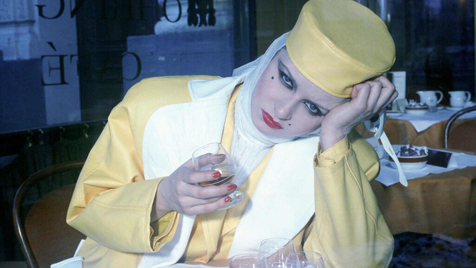 A woman sitting at a table drinking from a glass.
