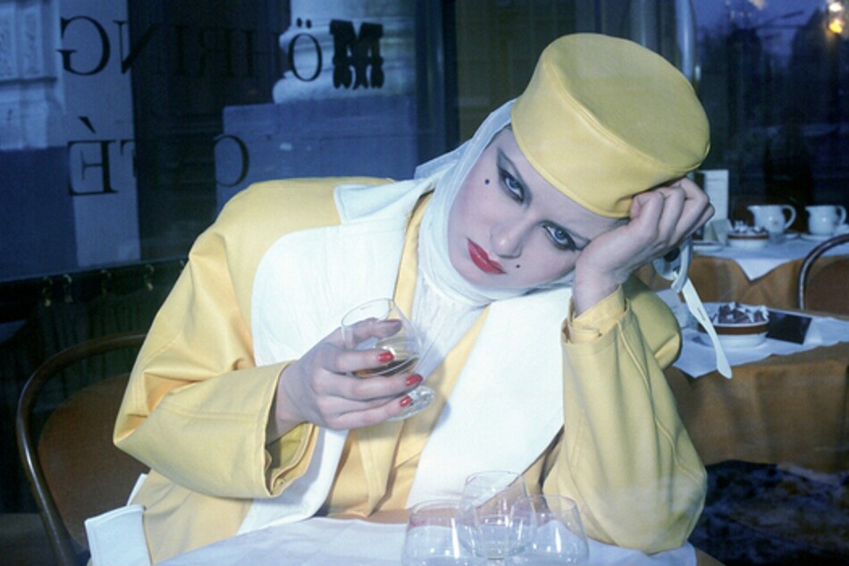 A woman sitting at a table drinking from a glass.