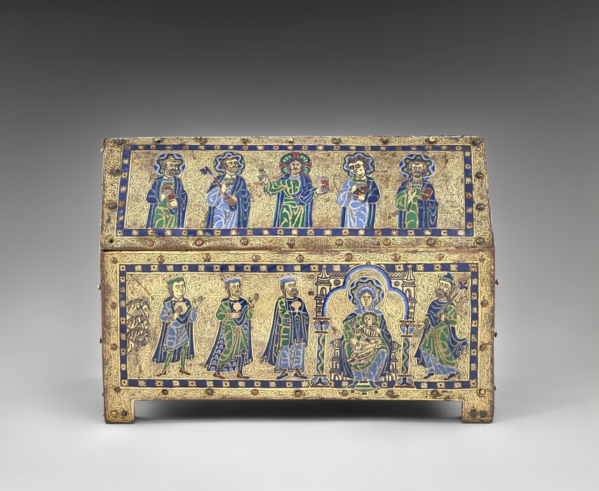 A free-standing, gold, enameled, rectangular box has a triangular top like the roof of a house, and the box rests on a short, square foot in each corner. In this photograph, we look onto one long side and the short side to our right is angled toward us, so we see the panel there, too. Along the long side, five people are shown from the waist up in the upper, roof-like panel and six more line up on the panel below. The skin of every person is gold, and all wear robes and garments in lapis or sky blue, spring green, yellow, and white. The area around the people is also gold, and each panel is encased by a royal-blue band dotted with stylized stars at regular intervals. Each panel is then lined with small, button-like rounded bosses around its edges. In the upper panel, all of the men except the second from the right have beards, and all have halos with wavy bands of blue, green, yellow, and white. The man to our left holds a book and his neighbor a skeleton key the length of his arm. The man at the center holds up a book with his left hand, on our right, and raises the index and middle fingers of his other hand, held up at shoulder height. The two men to our right also hold books. In the panel below, three horses’ heads peek in from the left edge, creating a vertical band, and three crowned men line up, holding gold vessels and looking toward a woman seated in a throne with a child on her lap. The woman has a halo made with a wavy pattern of blue, yellow, green, black, and white. Her throne is flanked by columns, and the area around it is edged with bands of white, light, and dark blue. The baby wears gold, has a halo, holds a book in his lap with his left hand, and raises the first two fingers of his other hand toward the three men. The final person in this panel wears a hat, holds a scepter topped with a fleur-de-lis, and gestures at the woman and baby. The head and shoulders of a haloed person is visible along the short side of the box, which is angled sharply away from us. The gold between all the people and bordering each panel is intricately carved with tiny flowing organic lines and swirls.