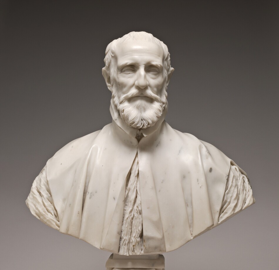 This free-standing, white marble sculpture shows the head, shoulders, and upper chest of a balding, bearded man. In this photograph, his body faces us and he looks straight ahead. Bushy eyebrows arch low over deeply set eyes, and his forehead hollows inward at his temples. He has high cheekbones and the skin of his cheeks draws slightly in. His thin lips are set in a straight line within a full beard. His high-necked robe falls slightly open over his chest and is cut also away over the shoulders to show the crinkled fabric of the garment beneath. The bottom edge of the sculpture curves upward in a very shallow U across the bottom, and is supported by a square pedestal foot decorated with scroll designs. The background behind the bust lightens from charcoal gray along the top edge to pale gray across the bottom, and the sculpture casts a shadow behind its base.
