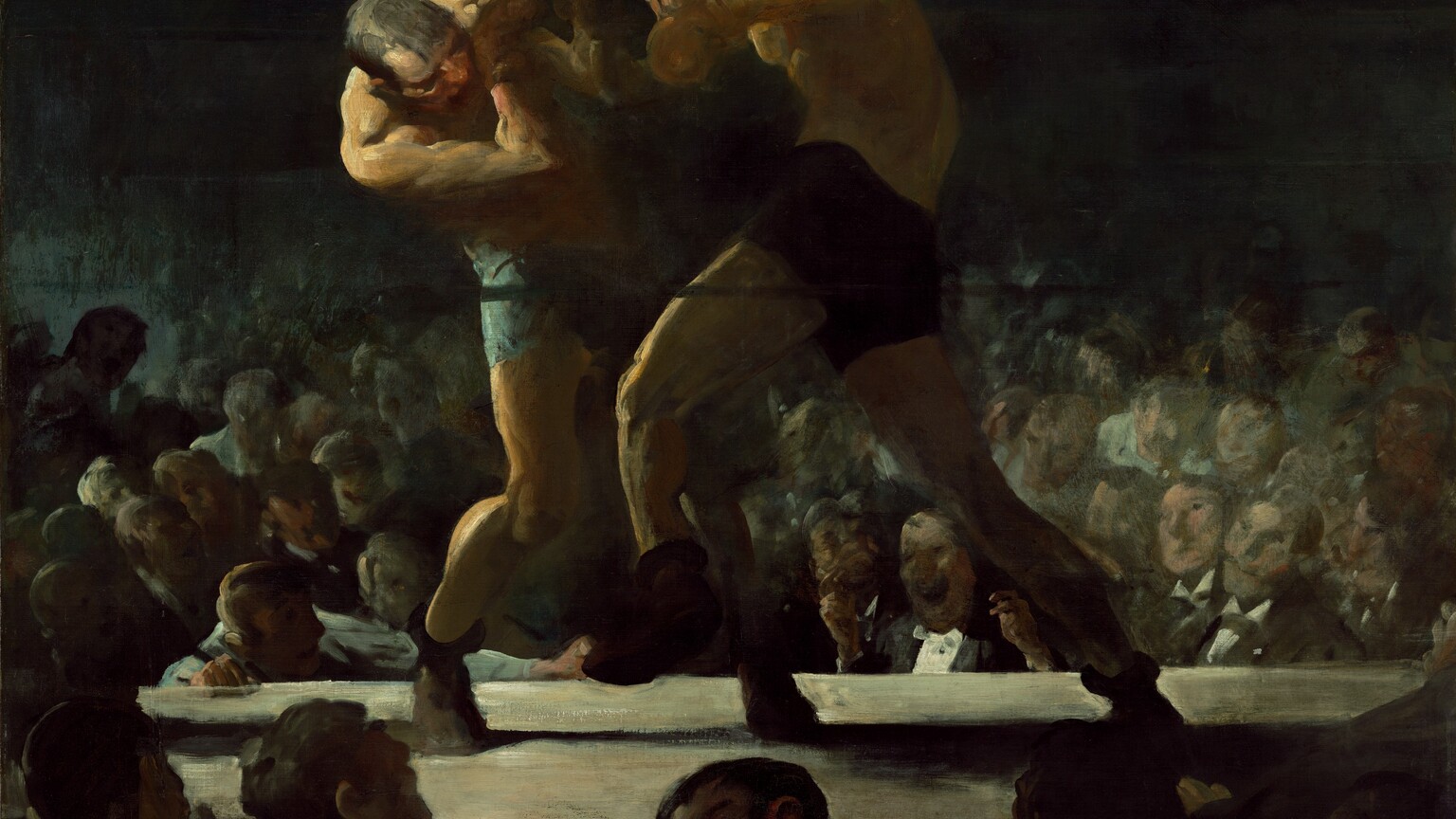 Two men wearing brief-like shorts, shoes, and boxing gloves curl toward each other as they grapple in the middle of a boxing ring in this horizontal painting. We look at the ring from across the heads of the crowd below and around us. The platform of the boxing ring comes about a quarter of the way up the canvas so the boxers themselves nearly brush the top edge of the composition. The boxer on our left has pale, peach skin and wears light blue shorts. He curves to his side as he dips his head and right shoulder toward us in a defensive position, arms shielding his face. To our right and in the center of the composition, the opponent has an olive-toned complextion. He wears dark shorts and is shown in mid-punch with his left leg raised to step forward. His back curves like a comma as his right arm comes forward with the punch. Bright light, like a spotlight, illuminates the men from our left so even the right sides of their bodies are lost in shadow. The crowd around us is backlit but one grinning man turns to look over his shoulder at or beyond us. The arena across the boxing ring is also plunged into deep shadow, so only the faces in the first few rows are visible before being swallowed in darkness. In fact, the top third of the canvas behind the boxers is black. The faces of the men in the crowd across from us are loosely painted, sometimes with only a few strokes to capture features. Individual features are mostly obscured but one face near the center, between the legs of the attacking boxer, is split wide in an exaggerated grin. That man wears a white tuxedo shirt and black jacket, and raises both hands, as if ready to light a cigar.