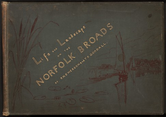 This muted, celestial blue, wide book cover has gold text and a drawn illustration of marshlands and sailboats. The text is oriented at an angle between the lower left and upper right corners. It reads, “Life and Landscape on the NORFOLK BROADS BY P.H. EMERSON and T.F. GOODALL.” In dark brown, cattails rise along the left edge, near the book’s tan-colored spine, and two boats sail away from us toward a harbor town to the right. The spine and cover are worn and scuffed, and there are a few stains.