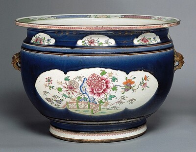 This is an ornate, decorative vessel resembling a large ceramic bowl or pot. Its surface features intricate floral designs painted in shades of pink, red, and orange, with hints of green leaves and a small brown fence around the flowers, all set against a white background. The main body of the vessel is a deep cobalt blue color and has a smooth, shiny surface. The vessel has small, golden-toned handles on each side.