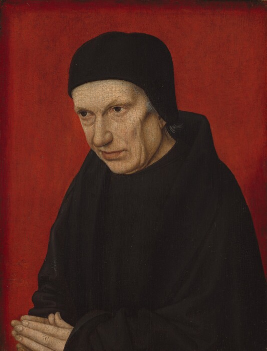 Shown from the waist up against a vivid red background, a pale-skinned, cleanshaven man looks off to our left in this vertical portrait painting. His body is angled to our left, and his head tilts down so he looks in that direction from under faint eyebrows. He has bags under brown eyes, sunken cheeks, and soft jowls. He has a rounded nose and wide chin. His pale pink lips are closed and the far corner appears to be pulled slightly back. A close-fitting brimless black cap nearly covers his gray hair, and he wears an inky-black cloak over a black robe. His hands are together in prayer in the lower left corner of the panel, and the background is scarlet red.