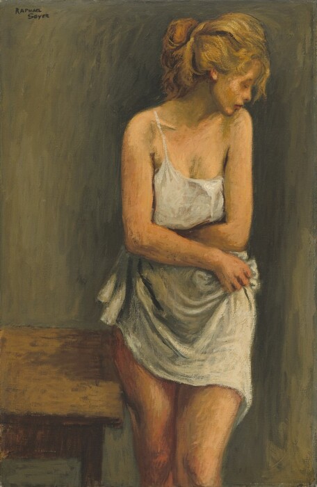 Shown from the knees up, a pale-skinned woman stands and clutches a white cloth to her body in this loosely painted, vertical composition. Her body is squared to us, but she turns her head to our right so that chin nearly touches that shoulder. Her face is tipped down, and her eyes are closed. She has a snub nose and full pink lips. Her long blond hair is pulled loosely up and back, and loose strands frame her face. She stands with her arms across her torso and one knee pushed a little forward. One spaghetti strap of her white tank top is looped over her shoulder, and the other has fallen down and off the other. She grips the white fabric around her waist and across her hips. A wooden table touches the side of her leg to tour left. The background is painted with streaks of olive and dark green. The artist signed the top left corner, “Raphael Soyer.”