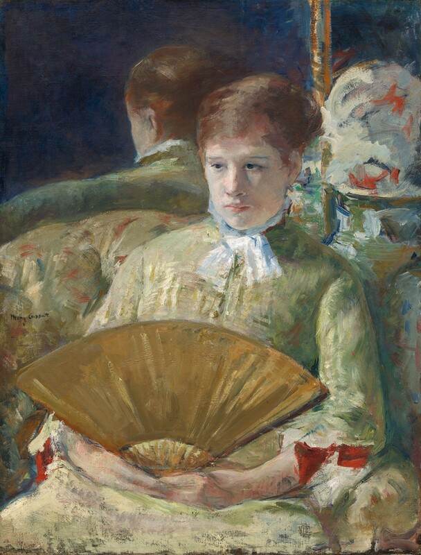 Shown from the hips up, a pale-skinned woman holds an open, gold-colored fan in her lap in this vertical, loosely painted portrait. Brushstrokes are visible throughout, especially in the clothing and background, so some details are indistinct. The woman’s body is angled slightly to our left, and she looks off in that direction with her chin pulled in. Her dark eyes seem unfocused under faint brows. She has an oval face with a straight, flaring nose, and her full, pale pink lips are closed. Her brown hair is pulled back, and she wears a white scarf tied under her chin. Her high-necked dress is painted with strokes and dabs of celery green and butter yellow and is shaded with mauve pink. The cuffs are scarlet red where they fold back over her forearms. The woman sits on an upholstered sofa with a rounded back, painted in similar shades of pale green and yellow with touches of red. The back of the sofa and the woman’s head are reflected in a framed mirror just behind the couch. The area in the top right corner of the composition is especially loosely painted but strokes in white, red, green, and blue. The artist signed the painting near the woman’s shoulder to our left: “Mary Cassatt.”