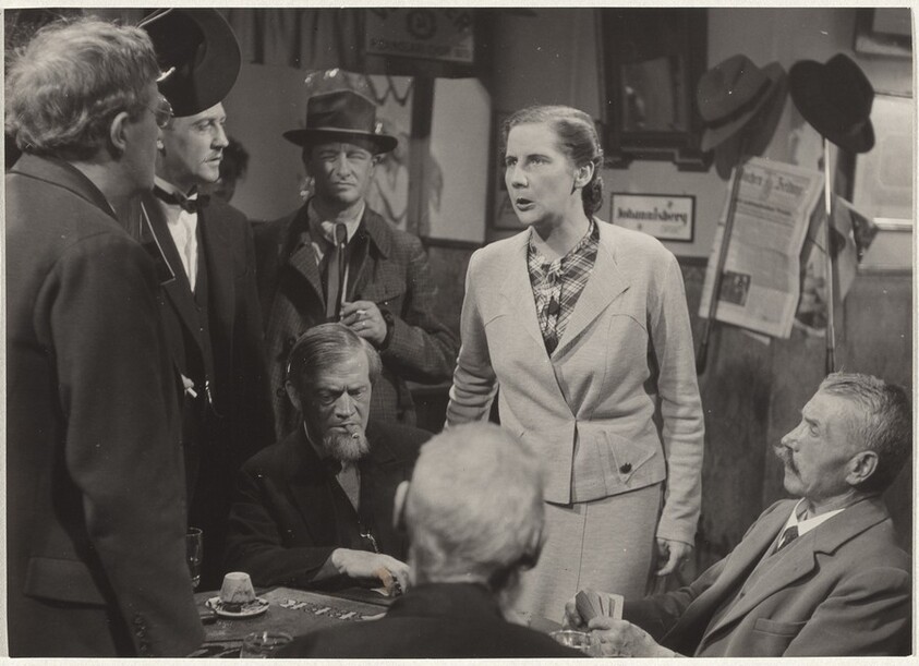 Woman standing over cardplayers--Filming