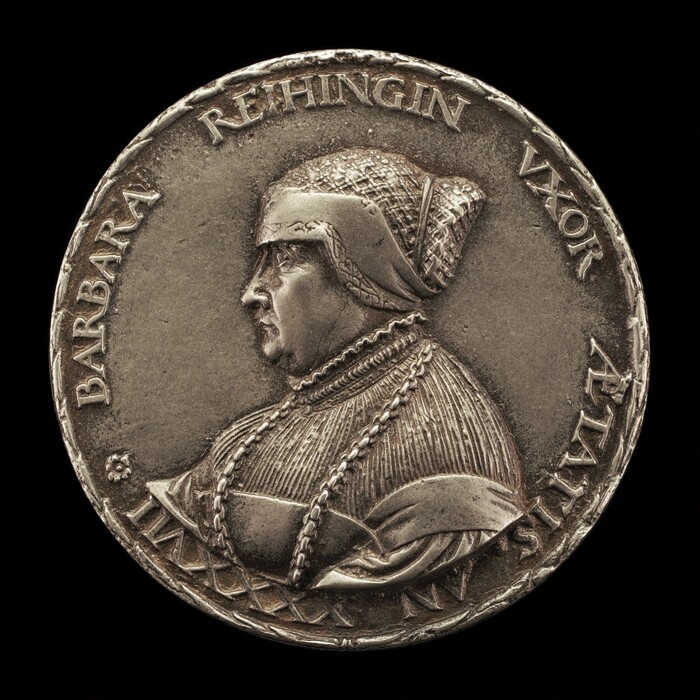 The sculpture depicts a profile of a woman named Barbara Rehingin. She is shown facing left, wearing a headdress with a textured pattern and intricate clothing with layered textures and ornamentation, including what seems to be chains or cords. The sculpture is colored metallic silver, indicating it may be made of silver or a similar alloy. Engraved text surrounds her portrait on the round surface. The piece showcases detailed craftsmanship and a dignified style within a circular form.