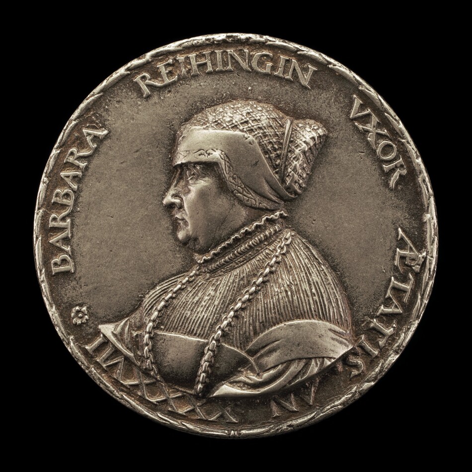 The sculpture depicts a profile of a woman named Barbara Rehingin. She is shown facing left, wearing a headdress with a textured pattern and intricate clothing with layered textures and ornamentation, including what seems to be chains or cords. The sculpture is colored metallic silver, indicating it may be made of silver or a similar alloy. Engraved text surrounds her portrait on the round surface. The piece showcases detailed craftsmanship and a dignified style within a circular form.