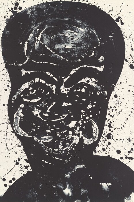 The image shows bold, swirling lines and splatters of black ink on a white background, creating an abstract composition. The central shape resembles a face with large eyes and a broad smile. The design may evoke a mask or a stylized representation of a human face, with the splatters adding a dynamic quality to the piece.