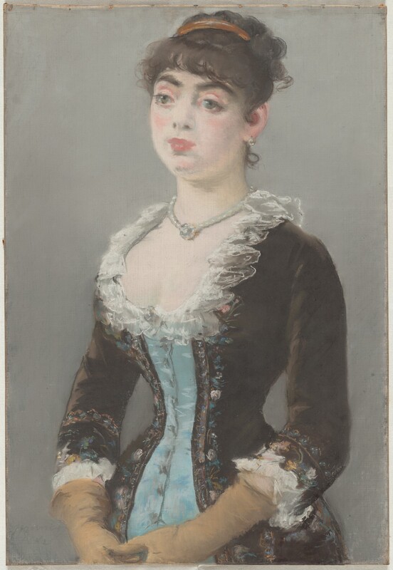 Shown from the hips up, a pale-skinned woman wearing a tightly corseted dress looks off to our left in this vertical pastel drawing. The portrait is loosely sketched with blended areas, giving it a soft look. The woman’s body is angled to our left, and her hands touch in front of her lower belly. She looks off with large, wide set, slightly bulging green eyes under dark brows. She has a round face, full pink lips, and the suggestion of a dimple in her chin. Her dark brown hair is pulled up under a gold band, and bangs curl across her forehead. A short, delicate ringlet curls up the nape of her neck. She wears a light-colored, round earring in the ear we see and a string of pearls, which may hold a round jewel that rests in the hollow of her throat. Her dress is powder blue down the front and coffee bean brown to either side and on the sleeves. The edges of the brown sections are lined with flowers drawn loosely in shades of pastel pink, blue, yellow, and green. The low, curving neckline is edged with white ruffles, and the waist is cinched to an almost startling degree. The sleeves come down just past her elbow, and the cuffs are also lined with white ruffles. Long, tan-colored gloves stretch back to the cuffs. The background is fog gray. The artist signed and dated the pastel faintly in the lower left corner, “Manet 1882.”