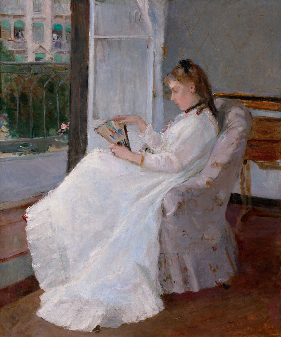 A young woman with pale peach skin and light brown hair sits in profile facing our left in an upholstered chair in this vertical painting. The chair and woman take up most of the composition so seems close to us. She wears a long-sleeved white dress that sweeps to the floor, with black ribbons around her neck and atop her shoulder-length ringlets. The dress has small ruffles at her throat and a deep flounce at the bottom. She gazes down at the partially open fan she holds on her lap. The fan is touched with spots of pumpkin orange, plum purple, and royal blue on a beige background. Loose, swirling brushstrokes in golden tan and bright white against an ivory background suggest that the chair is upholstered with a floral-patterned fabric. A wooden desk or table is pushed against the wall behind the woman to our right and to our left, a white door, covered by a white curtain, opens onto a balcony with a wrought iron railing. Across the street, a couple of people lean out of open windows covered by turquoise-blue awnings on a cream-colored building.