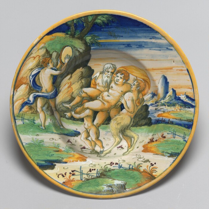 This is a painting of a mythological scene on a decorative plate. The scene depicted involves several figures engaged in an active, dynamic composition. The central figure is supported or carried by several other figures along a landscape filled with vibrant colors, including greens, blues, and warm earth tones. The background features an idyllic landscape with trees and rocky formations under a sky exhibiting gradations of blue and orange hues. A figure to the left appears to be playing a musical instrument. This is in the style of Renaissance majolica pottery, encompassing mythological and classical themes painted with vivid colors on ceramic ware.
