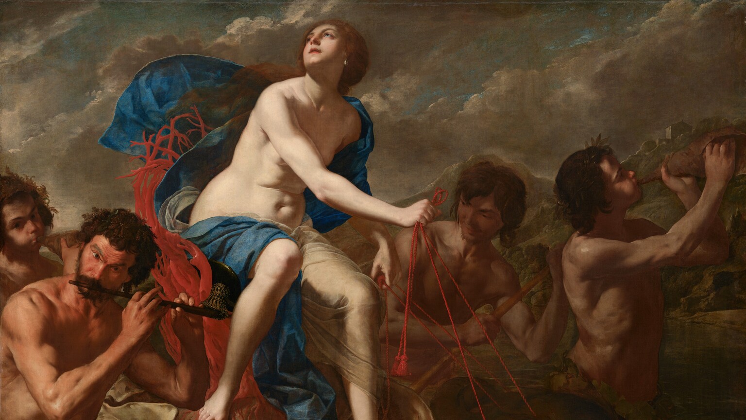 A nearly nude, pale-skinned woman rides an oversized seashell being pulled by stylized dolphins in this horizontal painting. Four muscular, tanned men with dark, unruly curly hair surround the shell and play music. The woman sits on a seat made by twisting red coral with her body angled to our right. She turns her face up and to our left, to the sky. She has dark eyes and brows, a heart-shaped face, a cleft in her chin, and her pink lips are parted. Her auburn-brown hair appears gathered at the base of her neck and long tresses lift in the breeze over her right shoulder, to our left. A teardrop-shaped pearl hangs from the ear we can see. A celestial-blue cloth and a translucent white veil wraps over one shoulder and flutters behind her. The cloth then drapes across her back and over her thighs, exposing her soft tummy and rounded hips. The fish-like dolphins pulling the shell have rounded heads and black, glassy eyes. Short fins run the length of their curved backs over dark, olive-green skin. The woman guides them using red, twisted cords looped through their mouths. A pair of musicians are to each side of the shell. To our left and in the lower corner, one man holds a flute to his lips. The outer corners of his eyebrows arch up under a lined forehead. A ring of broad leaves wraps around his waist. Another man behind him blows with cheeks puffed into a shell as he looks at us. In the pair to our right, on the far side of the shell, one man holds a stick, perhaps guiding the vessel, while another, at the front of the grouping, blows into a shell. The man at front wears rings of leaves around his head and waist. The scene is lit starkly from our left, illuminating the woman and casting the rest into shadow. The water around the group is dark, pine green. Rocky mountains dotted with trees and buildings rise in the distance. Ash-gray clouds create diagonal bands moving up and to our right against a muted blue sky.