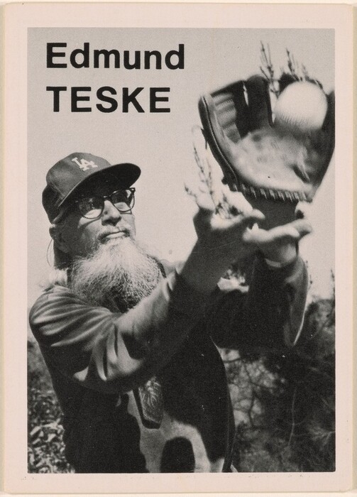 This is a photograph of a baseball glove catching a ball. The image shows a baseball glove held up, preparing to catch an incoming baseball. The background features tree branches, indicating an outdoor scene. The photograph has a grainy, high-contrast quality. The text on the image reads "Edmund TESKE".