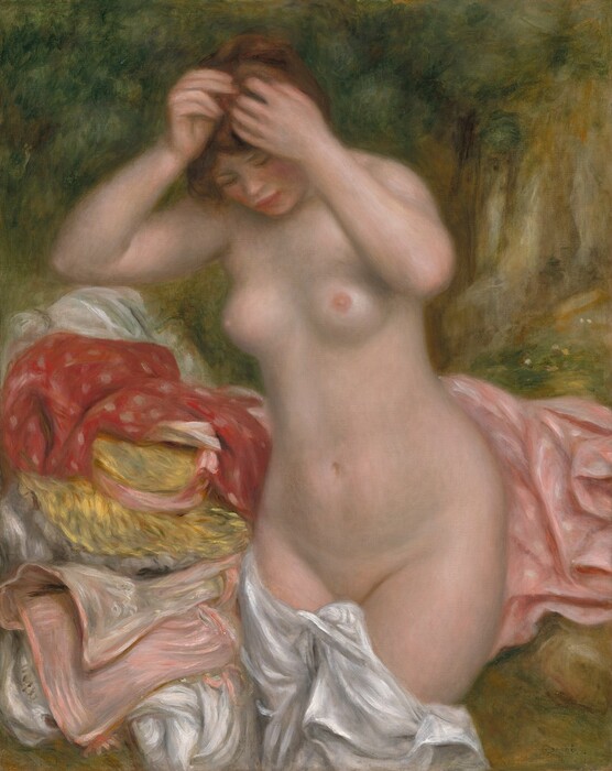 Shown from the knees up, a nearly nude, young woman with pale pink skin stands with her hands on her upswept, chestnut-brown hair in front of a pile of cloth, probably clothing, in this vertical painting. Blended brushstrokes give the painting a soft, almost blurred look. She stands with her body angled slightly to our left and her head tipped forward under her hands, which work in her hair. Her cheeks are flushed and her wide, pink lips are closed. Her round breasts are firm, and a piece of bright white fabric is bunched around her upper thighs below a smooth pubic area. Garments in the pile of fabric behind her are petal pink, vivid white, ruby red, and buttercup yellow. The area behind and around the woman and fabric is loosely painted with sage green, caramel brown, and golden yellow. Touches of yellow on a field of green to our right suggest grass and flowers. The artist signed the work with dark paint in the lower right corner: “Renoir.”