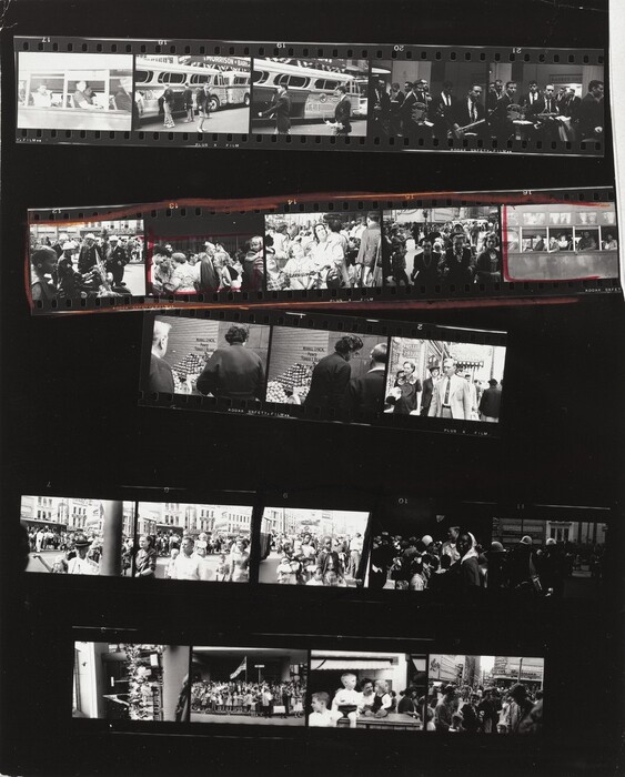 This contact sheet shows five strips of black and white film arranged on a black background. The first of five frames on the top strip shows people on a bus taken from outside the bus. The next two frames show young men wearing uniforms outside a bus, and then two frames of men holding musical instruments. The second strip shows a Black woman looking to our right in front of a group of white police officers; then three frames showing groups of people before another shot of people on the bus. This strip is outlined in red and then the second and fifth frames are also boxed in red. The third strip is made of three frames, two of which show to people at a fruit stand. The third frame is of a man and woman walking toward us on a city street. The fourth strip also has five frames. The first four show crowds of people, but the fourth is noticeably darker. The fifth would be hard to make out if not for the photograph of the police officers above. In the four frames of the final strip are two shots of people gathered around an American flag, a group of children, and a group on a city street.