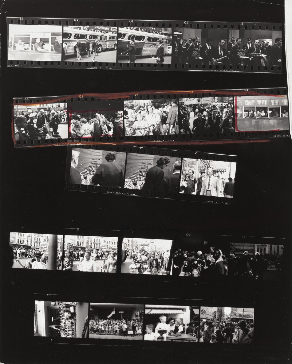 This contact sheet shows five strips of black and white film arranged on a black background. The first of five frames on the top strip shows people on a bus taken from outside the bus. The next two frames show young men wearing uniforms outside a bus, and then two frames of men holding musical instruments. The second strip shows a Black woman looking to our right in front of a group of white police officers; then three frames showing groups of people before another shot of people on the bus. This strip is outlined in red and then the second and fifth frames are also boxed in red. The third strip is made of three frames, two of which show to people at a fruit stand. The third frame is of a man and woman walking toward us on a city street. The fourth strip also has five frames. The first four show crowds of people, but the fourth is noticeably darker. The fifth would be hard to make out if not for the photograph of the police officers above. In the four frames of the final strip are two shots of people gathered around an American flag, a group of children, and a group on a city street.