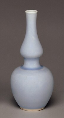 The sculpture depicts a vase with a bulbous lower body tapering into a slender neck. It is pale blue and made of ceramic. The vase has smooth curves and a glossy finish, exuding refinement and delicate craftsmanship. The neutral background accentuates its details and color.