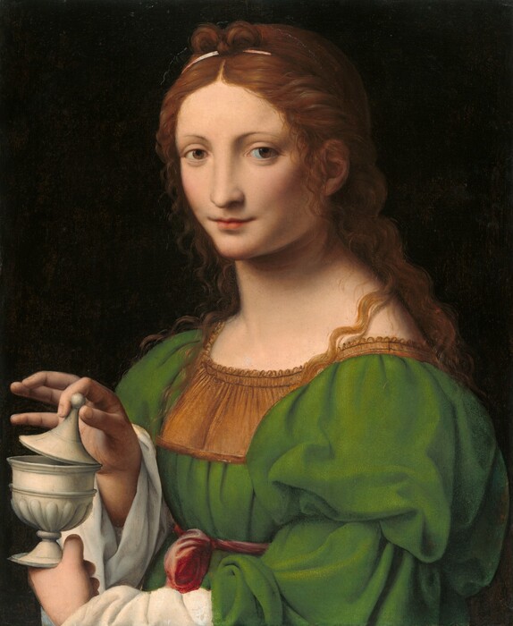 Shown from the waist up, a woman with smooth, pale skin looks out at us from the corners of her wide-set hazel eyes in this vertical painting. Against a nearly black background, her body is angled to our left and wavy, auburn hair cascades down her back. Her hair is arranged into a bow shape over a thin, pale pink ribbon, and delicate tendrils frame her face and fall over her shoulders. She has thin brows, and her long, straight nose is wide at the bridge. Her pale, coral-pink lips are closed in a slight smile. She is lit from our left so shadows engulf the corners of her eyes and lips, and her far cheek, to our right, is shaded. Her moss-green gown has a golden-brown panel across the chest and voluminous, puffy sleeves. The green sleeves fall back over the deep folds of the white garment she wears underneath, and the dress is tied with a pink sash just below her bust. She holds the flaring foot of an oyster-white lidded vessel, like a miniature urn, with one hand and tips the conical lid up with the other.