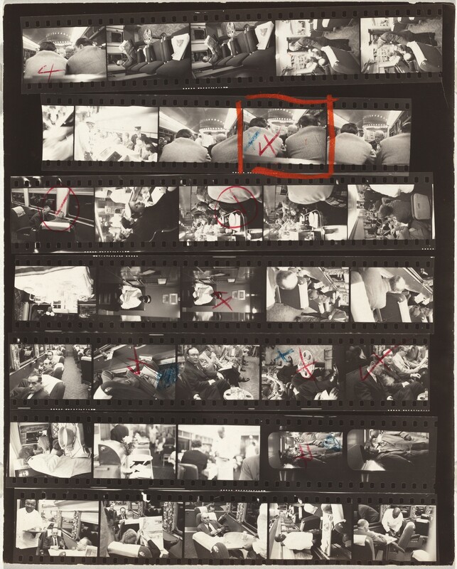 This photographic contact sheet has seven rows, each with five black and white images except for the second row down, which only shows four. The photographs were all taken on train cars. Most of the people are pale-skinned men wearing suits, but there are a few women wearing dresses and hats. They all sit in swiveling chairs or in the dining car. One uniformed conductor is light-skinned, and servers in the dining care are dark-skinned men wearing white uniforms. Eight of the shots have red check marks crossed out to make Xes, and some also have blue Xes. The marked pictures show a view of a bald man seen between the backs and shoulders of two hunched men; two men with receding hairlines sitting in chairs swiveled toward each other near the dark, mirror-like windows; a view down a counter in the dining car; a dark-skinned man wearing a white coat, conductor’s hat, and perhaps sunglasses, sitting alone; a close up of a newspaper and briefcase pinned between a swiveling chair and the side of the train car; a view of knees and legs, some crossed, along a row of seating; a man looking at us as others sitting in his row look down a papers; and the conductor and a passenger wearing a trench coat, both smoking pipes. One frame, another view of the bald man between the other two men’s shoulders, is marked in red and blue, and also outlined in a red box.