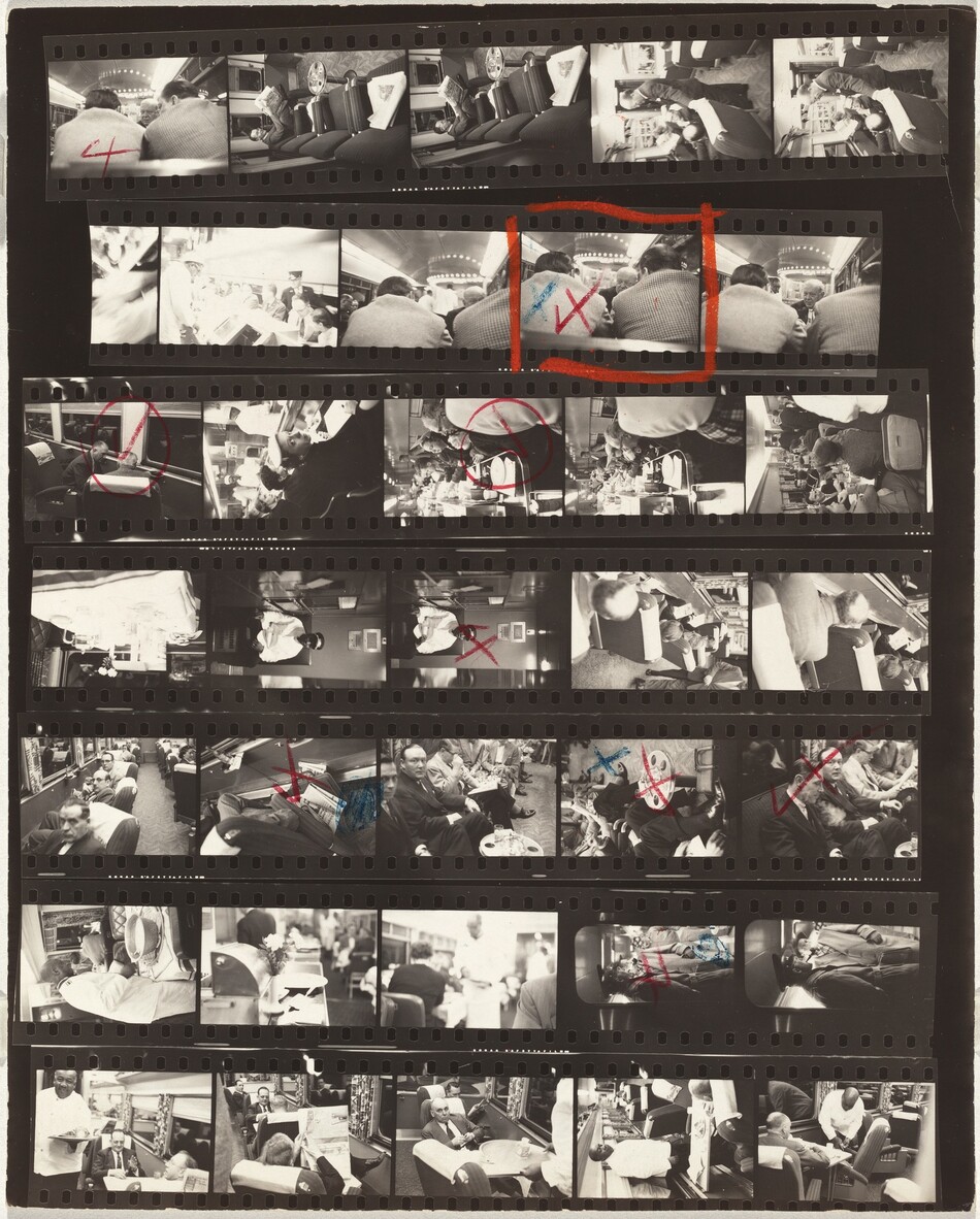 This photographic contact sheet has seven rows, each with five black and white images except for the second row down, which only shows four. The photographs were all taken on train cars. Most of the people are pale-skinned men wearing suits, but there are a few women wearing dresses and hats. They all sit in swiveling chairs or in the dining car. One uniformed conductor is light-skinned, and servers in the dining care are dark-skinned men wearing white uniforms. Eight of the shots have red check marks crossed out to make Xes, and some also have blue Xes. The marked pictures show a view of a bald man seen between the backs and shoulders of two hunched men; two men with receding hairlines sitting in chairs swiveled toward each other near the dark, mirror-like windows; a view down a counter in the dining car; a dark-skinned man wearing a white coat, conductor’s hat, and perhaps sunglasses, sitting alone; a close up of a newspaper and briefcase pinned between a swiveling chair and the side of the train car; a view of knees and legs, some crossed, along a row of seating; a man looking at us as others sitting in his row look down a papers; and the conductor and a passenger wearing a trench coat, both smoking pipes. One frame, another view of the bald man between the other two men’s shoulders, is marked in red and blue, and also outlined in a red box.