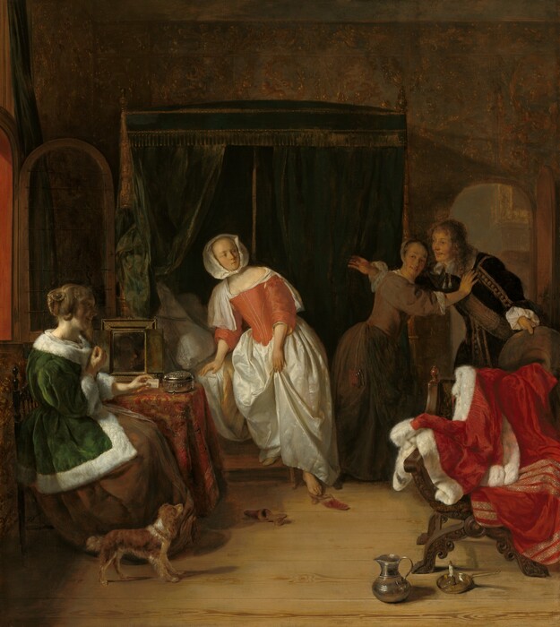 A young, smiling man bursts through the door of a dimly lit bedroom occupied by three women in this vertical painting. All four people have pale skin. The arched door is to our right and the man faces our left with his arms spread wide. He leans slightly forward as he holds the wide brim of his hat out by his left side, to our right. Shoulder-length chestnut-brown hair frames his face, and he wears a velvety brown jacket trimmed with tan stripes and pompoms down the front and along the sleeve we can see. A broad sash crosses his chest and tassels hang from his wide, white collar. Between us and him, a wooden chair is draped with a crimson-red cloak trimmed with white fur and bands of gold. A pewter pitcher and candlestick rest on the pine floor in front of it, near the lower right corner of the painting. The man is stopped at the door by a woman wearing a sable-brown gown with a tight-fitting bodice and a white cap on the back of her head. Her body faces the man as she leans toward him with her outstretched right hand resting on his shoulder, and she turns her smiling face back over her shoulder. Light from an open window on the left illuminates the woman in the center, who steps down from a bed enclosed by forest-green, velvet curtains trimmed with gold fringe and tassels. The curtains are parted behind her to reveal white pillows. She wears a long, gleaming white satin skirt topped by a tight-fitting coral-red bodice stitched with thin lines of gold. A white neckerchief covers her shoulders and is partially tucked into the bodice. Her head is covered by a white kerchief knotted under her chin. Her body faces us with one foot on a step stool, and the other foot reaches down to a gold and red shoe on the floor. Its mate lies nearby, pointing away from us. Her head is turned to our right to look at the man. She has a thin face with a high forehead, and small mouth is closed or pursed. Closest to us and near the lower left corner of the painting, the third woman sits alongside a small table under the open window. She wears a long, pine-green jacket trimmed with white fur over a brown skirt. Her auburn hair is partially coiled around her head, while some locks fall in bunched curls. She sits facing our right in profile with her back to the window, so her smiling face is mostly in shadow. Her left arm rests on the table, which is draped with a red and copper patterned cloth, and she holds a white comb in that hand. A mirror and round silver box sit on the table next to her. A small brown and white dog stands by her feet, its head tilted up to look at the others. The far wall of the room is covered with a faint pattern of golden brown vines and leaves against a forest-green background. The artist signed the painting on the face of the step leading up to the bed, “G. Metsu.”