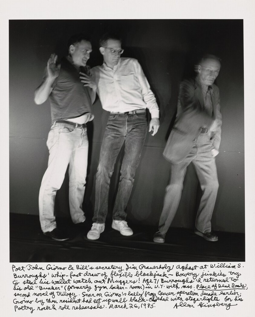 Poet John Giorno & Bill's secretary Jim Grauerholz aghast at William S. Burroughs' whip-fast draw of flexible blackjack- - Bowery junkies try to steal his wallet watch out Muggers! Age 71 Burroughs'd returned to his old "Bunker" (formerly gym locker-room) in N.Y. with mss. _Place of Dead Roads_, second novel of trilogy. Scar on Giorno's belly from cancer operation decade earlier; Giorno by then resident had set up wall black- clothed with stage-lights for his poetry rock & roll rehearsals. March 26, 1985.