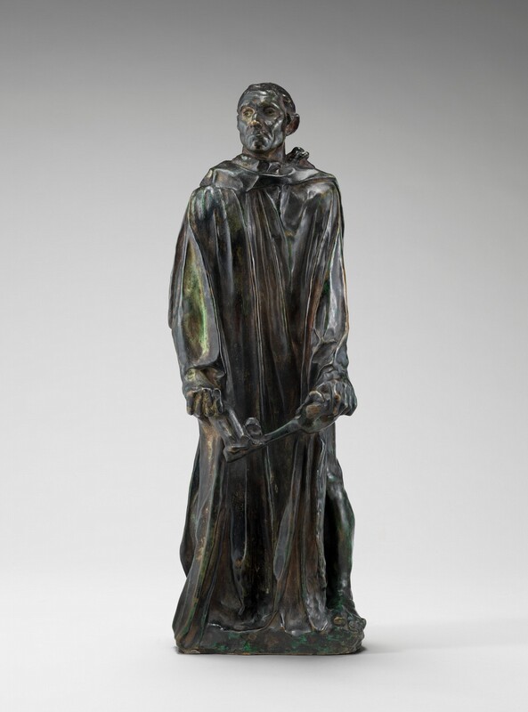 Cast in bronze, this free-standing sculpture shows a man with a gaunt face wearing a robe that falls in long, vertical folds as he holds an oversized skeleton key down in front of his thighs. In this photograph, the man’s body faces us but he turns his head to our left to look in that direction, his chin sightly raised. He has close-cropped hair, sunken eyes, hollow cheeks, a wide, square chin, and his thin lips are downturned. The long-sleeved robe drops heavily to his feet, and the toes of one bare foot peek out. A hint of a raised, round halter like a yoke around his neck shows from under his robe near his left shoulder, on our right. Most of the surface has a dark green patina except for a few lighter places, as on his sleeve to our left and in the thick drapes of his robe. A few areas are rubbed gold, including the tip of his nose and the knuckles of his hands.