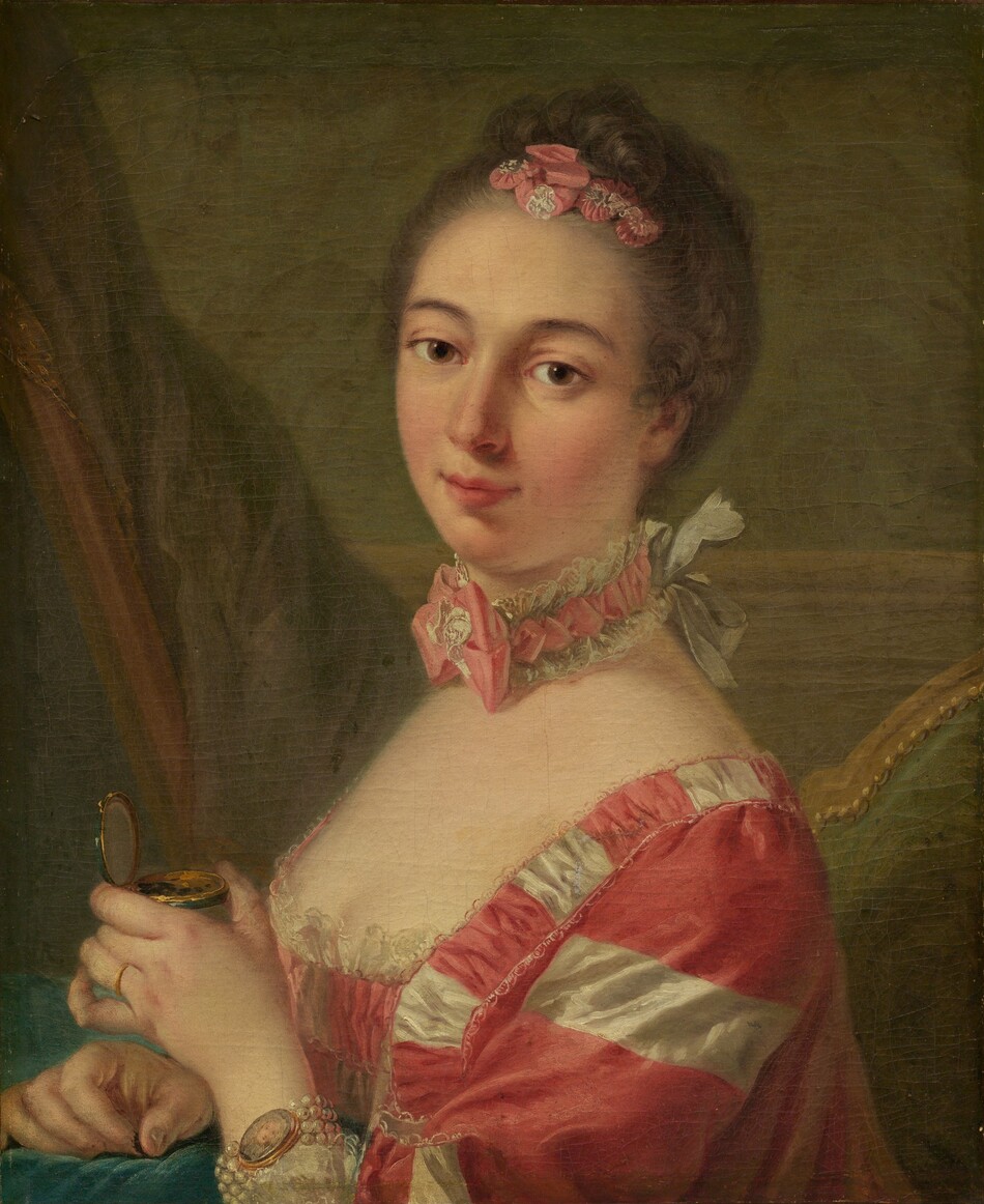Shown from the chest up, a woman with smooth, pale, peachy-toned skin wearing a carnation-pink and white gown looks at us from this vertical portrait painting. The woman’s shoulders are angled to our left, but she turns her head and tips it to our right to look at us with brown eyes under curving, gray brows. She has an oval face with a straight nose, a hint of a double chin, and her full pink lips are closed in a slight smile. Her ash-brown hair is pulled up and back and curls across the top of her head around pink and white ribbons pleated to resemble flowers. Her square-necked, low-cut bodice is lined with lace across her pale decolletage. The fabric is patterned with thinner white stripes and wider dark pink stripes. A choker tight around her neck has a pink ribbon edged with white lace and tied into a bow at the front of her throat. The necklace is tied on with a white bow at the back of her neck. She wears a gold ring on the fourth finger of her left hand, which is closer to us. On that wrist, four strands of white pearls hold a miniature oval portrait of a pale-skinned person. The woman holds a gold and emerald-green compact with that hand, and the other rests on an aquamarine-blue cushion or cloth in front of her at chest height. She pinches something brown between those fingers, and a few specks of brown are in the box. She sits in a wooden chair upholstered with moss green on the back. A curtain or other swath of muted purple fabric is to the left, and the wall behind her has chair-rail molding and is painted soft leaf green.