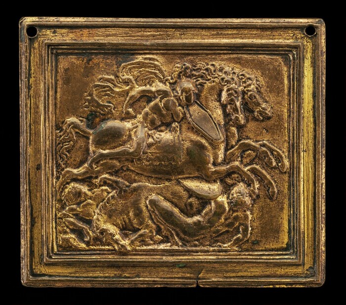 The sculpture depicts a horse and rider in motion, with a figure below the horse in a crouched position. The scene is set in relief on a square plaque. The sculpture appears golden in color with an aged patina. The intricate details of the horse's mane and the rider's drapery stand out against the flat background. The plaque is bordered by a raised frame and has two small circular holes at opposite corners.