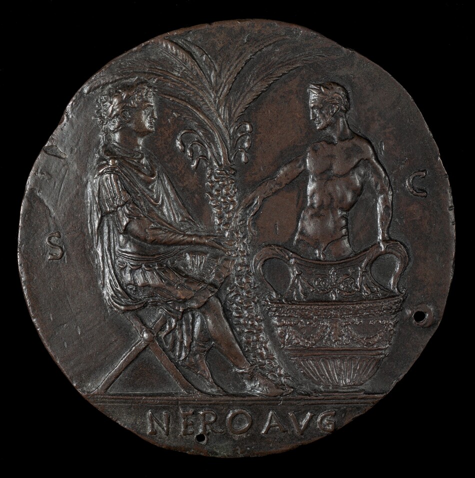 The sculpture on the ancient coin features two figures. On the left, a figure is seated on a folding chair, dressed in a classical toga or robe. Their hair is styled in wavy locks. On the right, a standing figure is shown leaning on a large amphora-like vessel with one hand and gesturing towards the seated figure with the other. Between the two figures is a tall palm tree. The sculpture is crafted from bronze, giving it a dark brown color with areas of lighter sheen. Surrounding the figures are inscriptions and markings, including "NERO AVG" at the bottom. The circular sculpture has two small holes, possibly for mounting.