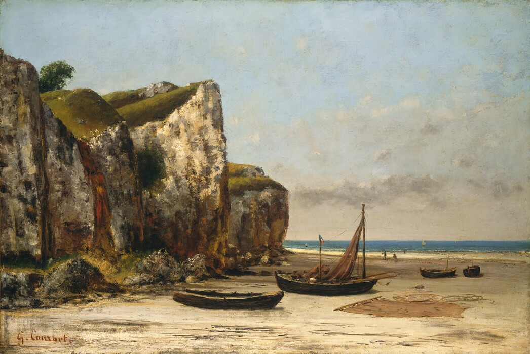 Towering, sheer cliffs loom to our left, over a sunny beach scattered with boats in this horizontal landscape painting. The chalky, rugged faces of the cliffs are dappled and streaked with olive green, dark brown, gray, rust red, and mustard yellow. The horizon comes a third of the way up the composition so the cliffs are outlined against the powder-blue sky, which is loosely veiled with wispy, cream-white clouds. The mossy tops of the cliffs are illuminated by sunlight from the upper left, and a solitary leafy tree leans into view between the two cliff-tops closest to us. Four empty, wooden boats sit on the flat, sandy beach below. We look onto the long sides of the two closest to us. One is stripped and appears dilapidated, while the one behind it has a ginger-brown sail attached to the mast in the prow. Two more wooden poles or oars jut out from the cockpit on either side of the mast. A small flag with horizontal bands of blue, white, and red flies from a short pole near the middle of the boat. A bundle the same color as the unfurled sail sits in the boat. Another sail is spread out on the sand to our right, and coiled ropes lie nearby. The two other boats are slightly further back on the right, with one angled to our left while we view the other straight on. There are two people a short distance beyond these boats. One faces our left in profile while the other sits on the sand looking toward the water. Thin trails of white delineate the low surf and a few sailboats drift by on the brilliant blue water. The artist signed the lower left, “G. Courbet.”