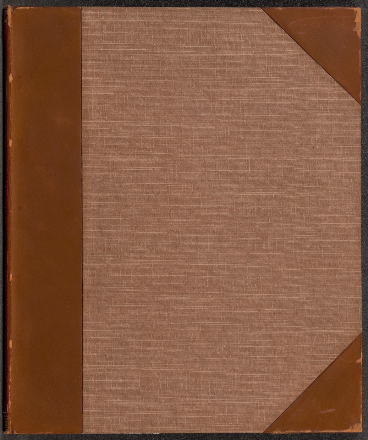 This is a photograph of a book cover. The cover features a textured fabric material in a neutral brownish tone, with reinforced corners and spine made of a smooth, slightly darker brown material resembling leather. The stitching pattern on the fabric gives it a subtle crosshatch design. The book cover does not contain any visible text, illustrations, or embellishments.