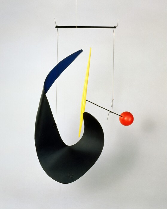 Three geometric structures are suspended with wire from a rod in this free-floating sculpture called a mobile. The supporting rod is black and hangs from the ceiling by a clear filament. To the left is a curved, twisting, C-shaped piece of sheet metal painted black on one side and cobalt blue on the other. To the right, a red ball and a yellow, toothpick-shaped shaft are connected by a second black rod. A wire connects the two rods so the ball and shaft balance to either side.