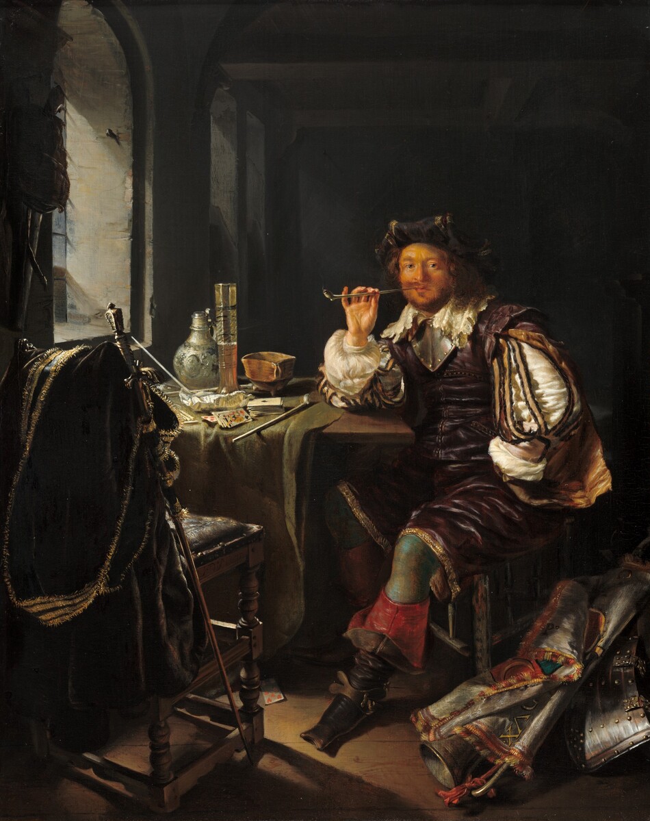 A pale-skinned, bearded man sits at a table set in front of a window and smokes a pipe in this vertical painting. Light pours in from the window and leaves much of the room behind the man in deep shadow. The man’s body is angled to our left, and he rests his right elbow, also to our left, on the table and looks steadily at us. The man has a round face with rosy cheeks and a copper-red beard. His dark, gold-edged hat rolls back away from his face, creating an upward flounce. His cream-white, lace-edged collar lies across his shoulders over a gorget, the piece of silver armor that encircles the neck and comes to a point over the chest. His plum-purple sleeveless jacket and loose, knee-length britches have a sheen. Voluminous white sleeves are covered with strips of black and golden yellow fabric, and yellow fabric flares like a mini cape behind the sleeve we see. The man wears a tawny-brown glove on his left hand, to our right. That hand rests on his hip with the palm facing out. He holds the long, white clay pipe to his lips with his other ungloved hand. A wisp of smoke rises from a burning ember at the end of the pipe. The man’s pants are edged with gold around the bottom hem, which fall loosely around teal-green stockings. His slouchy black boots have square toes, and the tops fall down to reveal crimson-red undersides. A brass band wraps across the arch of the foot closer to us, and a star-shaped spur projects off the back. The man sits on a three-legged stool with a triangular seat. More armor, a horn, and a banner with fringed edges lie in a heap in the bottom right corner of the painting. To the left, a playing card, a seven of hearts, lies face up near a second chair, this one wood with a seat upholstered in iron gray. A forest-green cloak edged with gold fringe is draped over the high back of that seat, and a staff with a metal finial leans against the cloak. The seat and stool face a table mostly covered with a sage-green cloth. More playing cards, three more white clay pipes, a tall glass of beer, a clay pot, and a white jug with a narrow silver lid sit on the table. A sack and perhaps a firearm hang on the wall to the left of the arched window, which is set in the thick gray wall. The floor is wood plank, and the space behind the man falls into shadow but appears to be empty. The artist signed the painting as if he had inscribed his name on the side of the chair with the cloak: “FvMieris.”