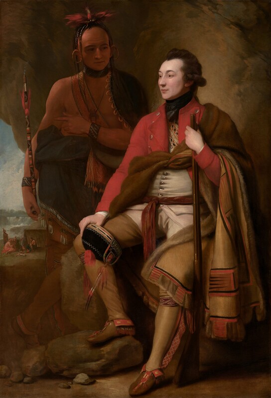 A man with pale white skin sits and a man with light brown skin stands in front of a cave-like, rocky outcropping in this vertical portrait painting. The light-skinned man closer to us has dark brown hair, and the light falls more strongly on him. He sits propped on or against a rock with his body angled to our left, and he looks off into the distance in that direction. He wears a scarlet-red overcoat, a white waistcoat, and moccasins. What appears to be an animal skin painted on the underside with red, tan, and black geometric patterns is tied around his chest and falls over his left arm, on our right. With that hand, he holds a musket like a walking stick. He also holds a black cap ornamented with beads and feathers on his other knee. The man with brown skin stands in shadow behind the other man, to our left. His body faces us, and he looks at the seated man. A dark cloak encircles his shoulders and is gathered around his waist. A strap crosses his bare chest and the strap, bracelets, and a feathered headdress seem to be beaded. Large gold rings curve from his earlobes up over his ears. A puff of smoke emerges from the top of the long, painted stick he holds, suggesting  it is a pipe. He holds his left hand, on our right, at his chest, and points subtly to our left, perhaps to the landscape seen through a break in the rocky outcropping. There, in front of a waterfall in the distance, a small group of people with light brown skin gather around a camp fire in front of a tent-like structure.