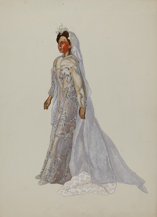 The image is of a person standing and facing slightly to the left. They have dark, wavy hair styled with a small floral headpiece. They wear a long, intricately decorated gown with beads and embellishments, made of a light, translucent fabric with a draped design, a fitted bodice, and long sleeves. They also wear a long lace veil extending down to the floor. The background is plain and off-white.