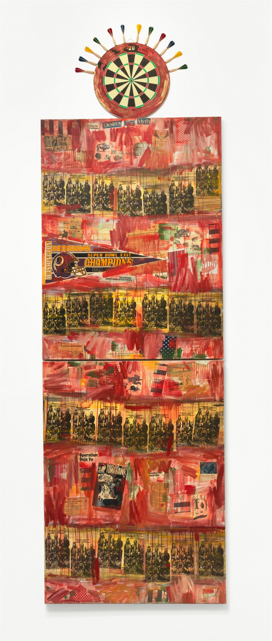 Two vertically oriented, rectangular canvases are stacked over each other, and a dart board is affixed to the uppermost edge. The canvases are collaged with newspaper articles, headlines, black-and-white pamphlets, cartoons, comic books, illustrations of animals like chipmunks and buffalo, and a triangular pennant celebrating the “Washington Redskins” as “Super Bowl XXVI CHAMPIONS.” Streaks and drips of red paint create horizontal bands across the panels, separated by bands streaked in yellow. Text is visible throughout, including the title of the pamphlet, which repeats across the composition: “Community Service and Interest Courses/Workshop.” Headlines include “The Heist,” “For People Who Inherited Brains Instead of Wealth,” “Defying the Stereotypes,” and “Destroy The Myth.” The comic is titled “Son of Tomahawk,” and fliers are titled “Help Locate Handicapped Indian Children” and “2nd Annual Flathead Reservation Culture Fair.” One piece of blue fabric with white polka dots is along the bottom edge of the top panel and a piece of red fabric with white dots is along the bottom edge of the lower panel. The outer band of the dart board is smeared with red, and darts with red, blue, yellow, or green feathers line the upper perimeter of the board.